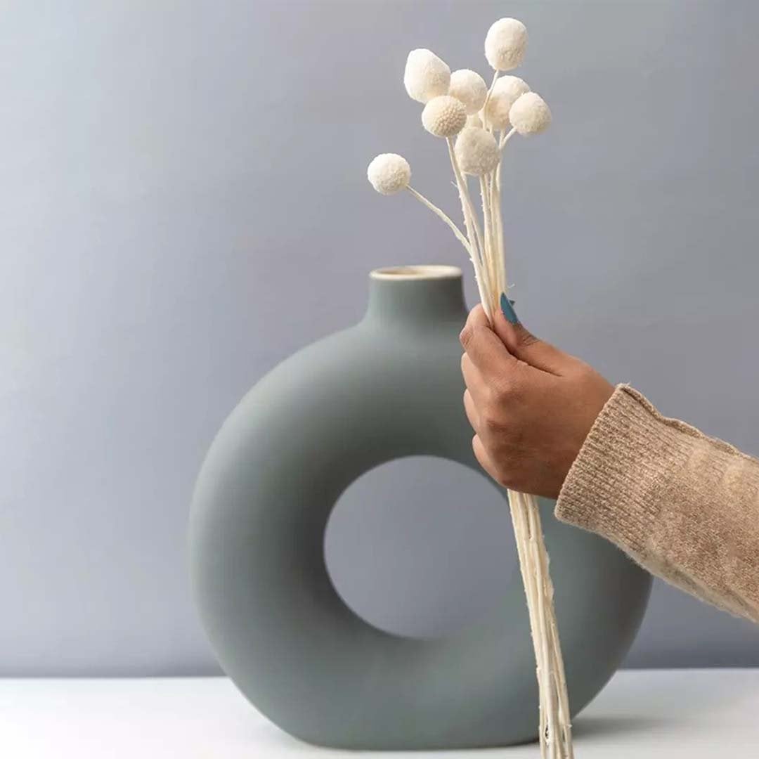 Modern ceramic ring vase in soft sage green held with dried floral stems on white background for minimalist home Decor styling.