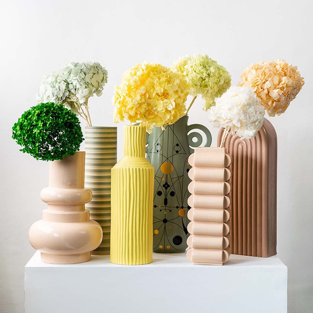 Set of modern ceramic vases in beige yellow and green with ribbed and geometric patterns styled with artificial flower decor.
