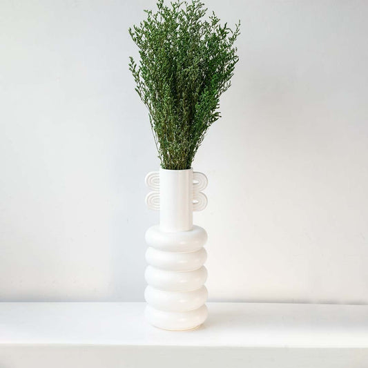 Green dried filler foliage styled in tall modern white ceramic vase against wall creating elegant lifestyle home decor.