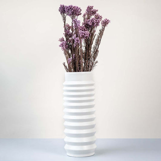Purple dried statice flower stems arranged in tall ribbed white ceramic vase elegant lifestyle floral home decor.