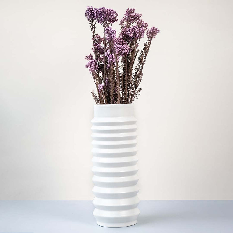 Purple dried statice flower stems arranged in tall ribbed white ceramic vase elegant lifestyle floral home decor.
