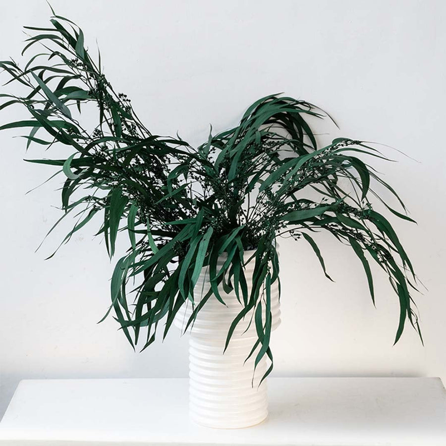 A long green artificial eucalyptus branch placed in a ceramic vase brings a calm earthy beauty to minimalist home styling.