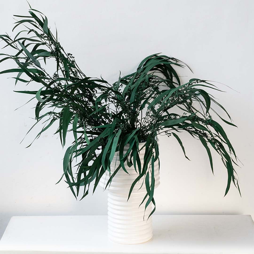 A long green artificial eucalyptus branch placed in a ceramic vase brings a calm earthy beauty to minimalist home styling.