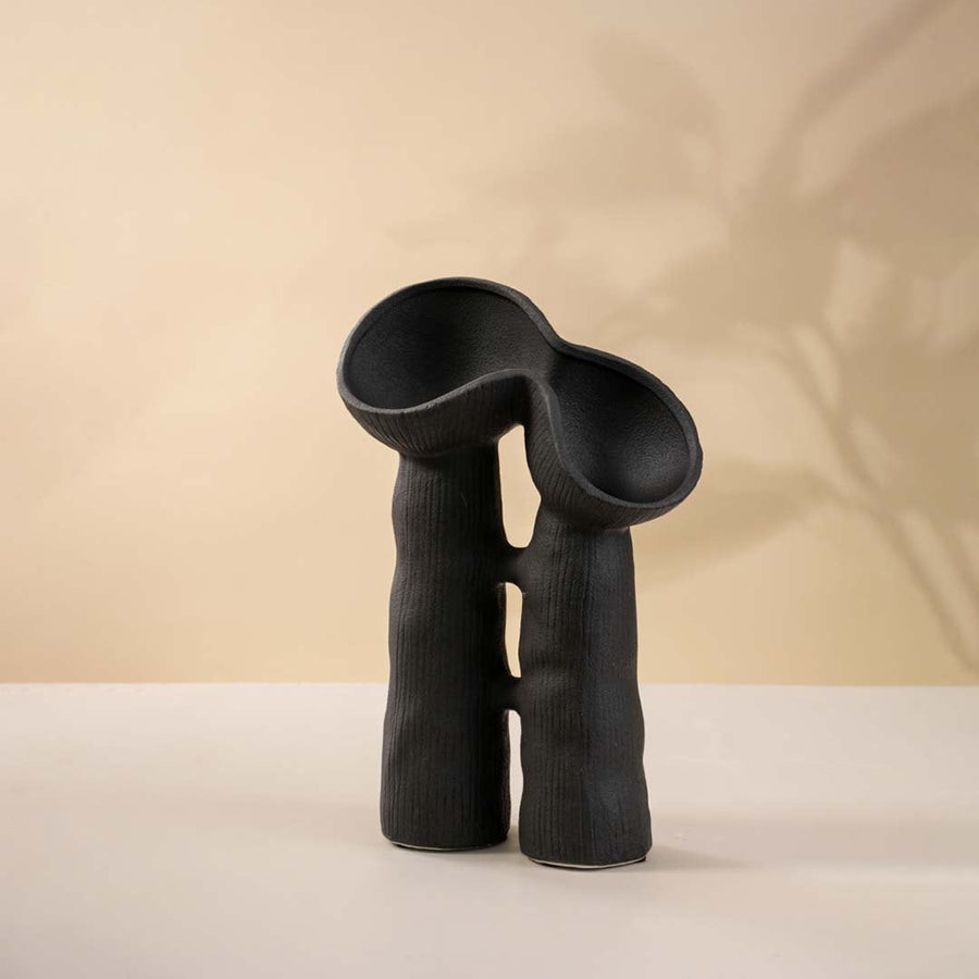 Handcrafted matte black ceramic vase with artistic form and two hollow sections against white backdrop.