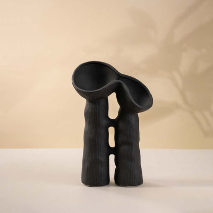 Contemporary black sculptural vase against white background to reveal textured detailing and artistic design.