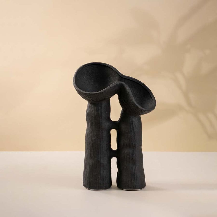 Contemporary black sculptural vase against white background to reveal textured detailing and artistic design.