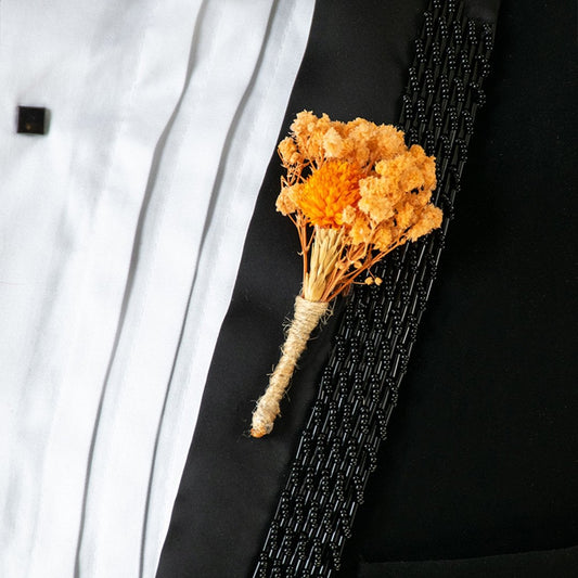 Closeup view of dried flower boutonniere with orange blooms tied in jute placed on black suit for elegant wedding attire.