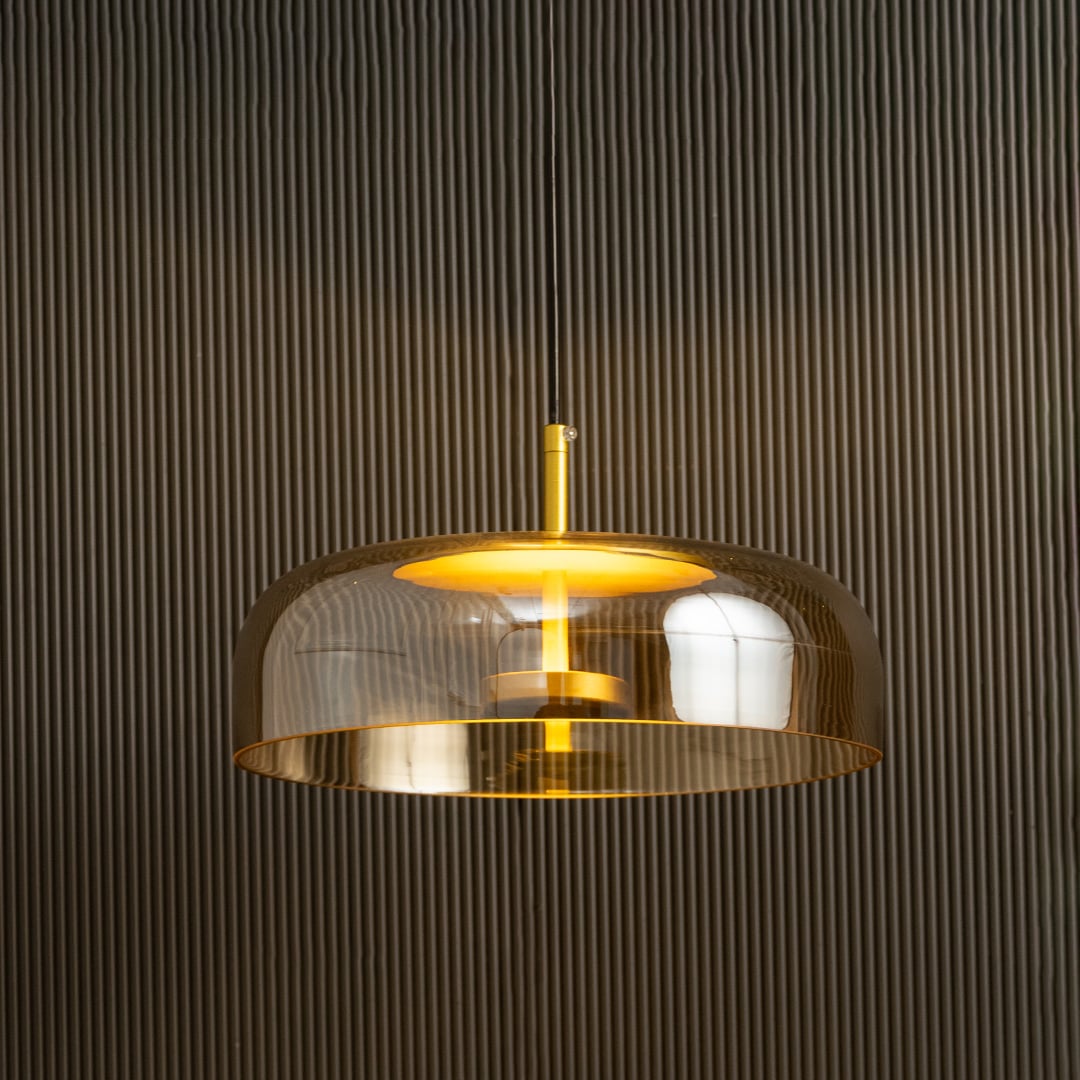 Amber glass pendant light with metal detailing casting a warm ambient glow imagined against a dark background creating a dramatic modern interior decor mood.