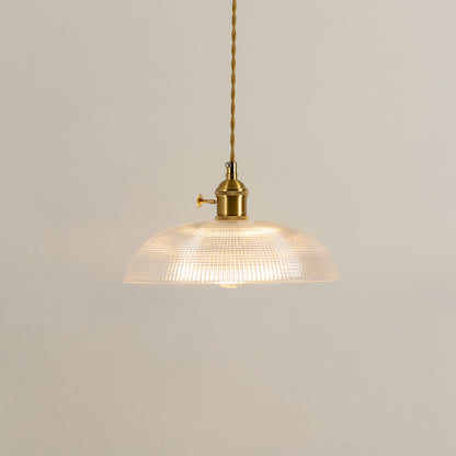 Illuminated clear ribbed glass pendant light with gold hardware creating soft ambient lighting indoors.