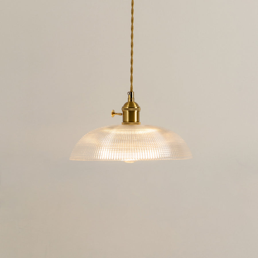 Illuminated clear ribbed glass pendant light with gold hardware creating soft ambient lighting indoors.