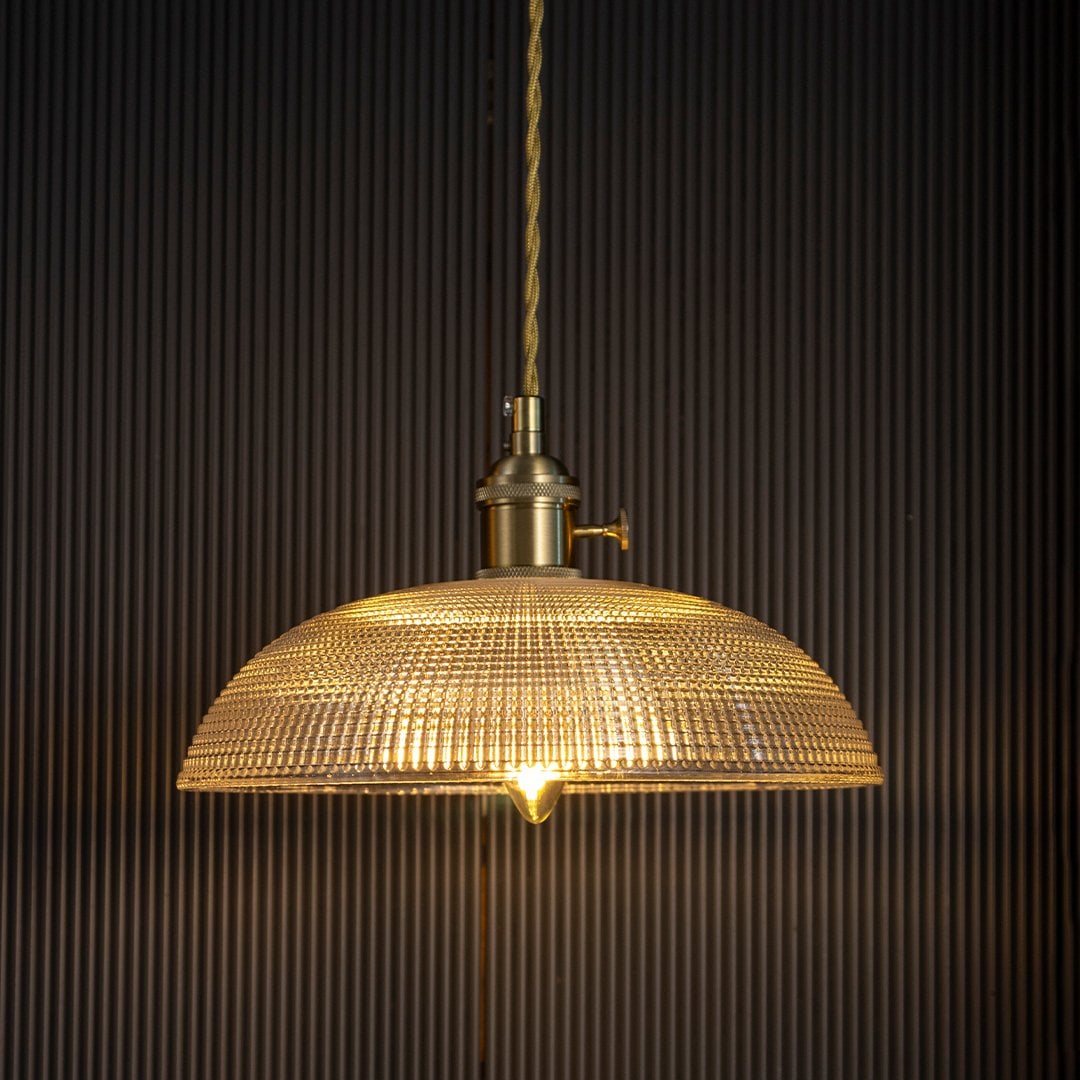 Clear textured glass pendant light with gold metal fittings casting a warm glow for elegant dining interiors.