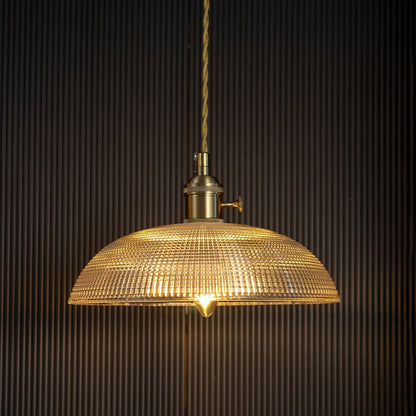 Clear textured glass pendant light with gold metal fittings casting a warm glow for elegant dining interiors.