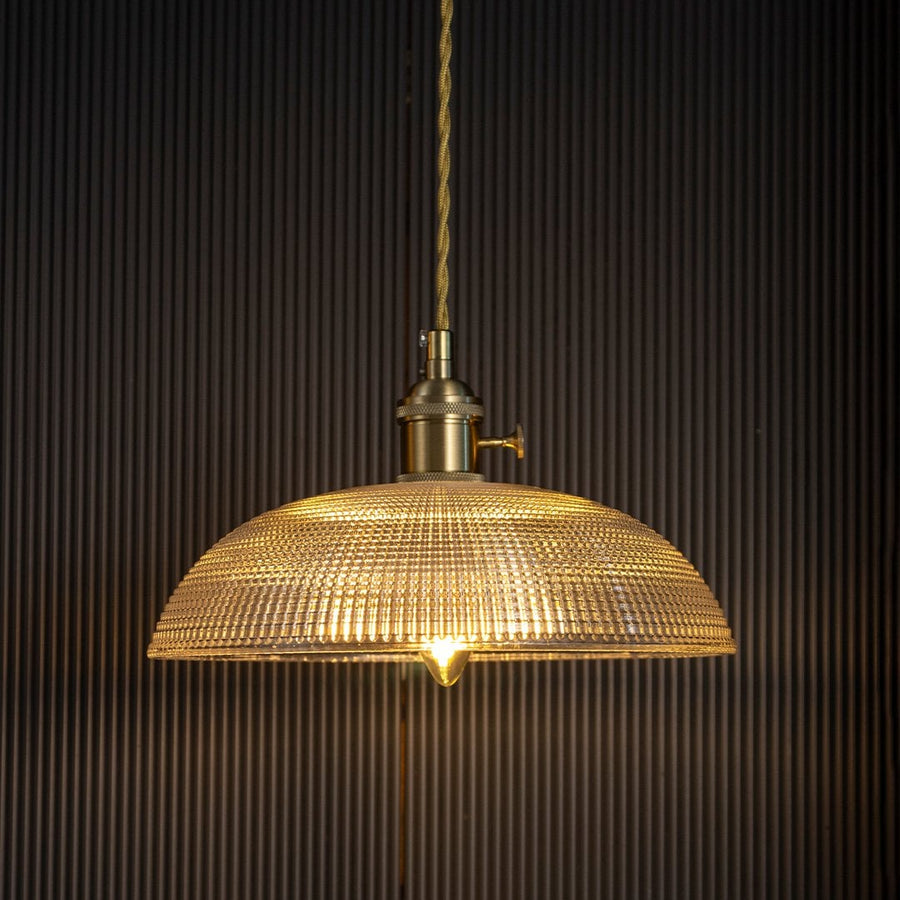 Clear textured glass pendant light with gold metal fittings casting a warm glow for elegant dining interiors.