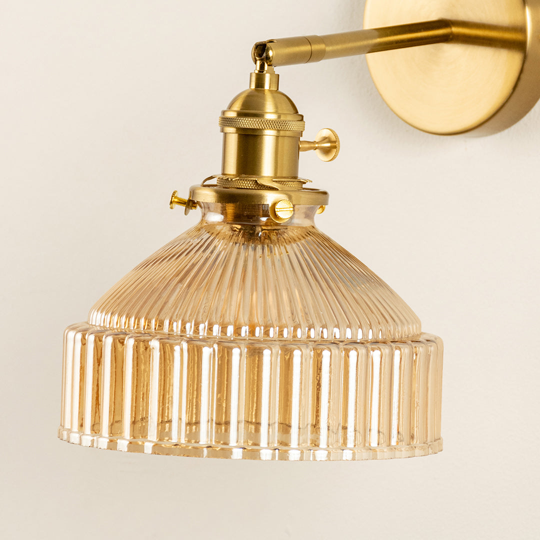 Closeup of gold metal wall light with ribbed glass shade showcasing detailed texture and premium finish for modern interior decor styling.