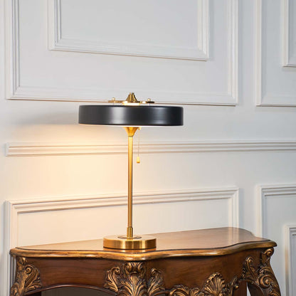 Black and gold metal table lamp with circular shade styled on a wooden console table offering contemporary decor lighting.