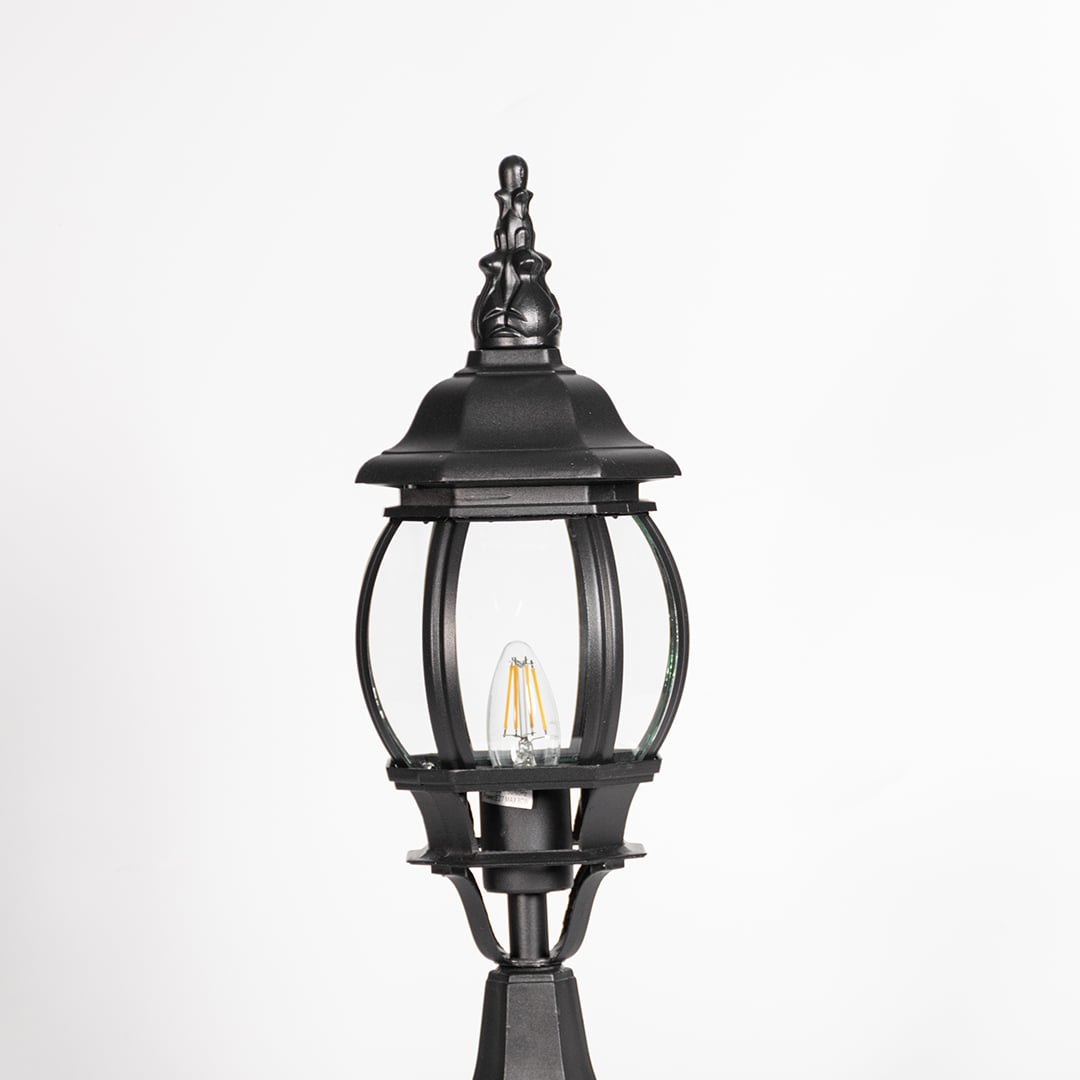 Closeup of decorative tall outdoor black pillar lamp with curved round glass panels and LED bulb showing vintage style.
