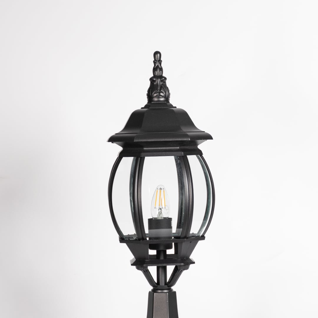 Closeup of decorative outdoor black pillar light with clear curved glass and LED bulb highlighting premium classic design.