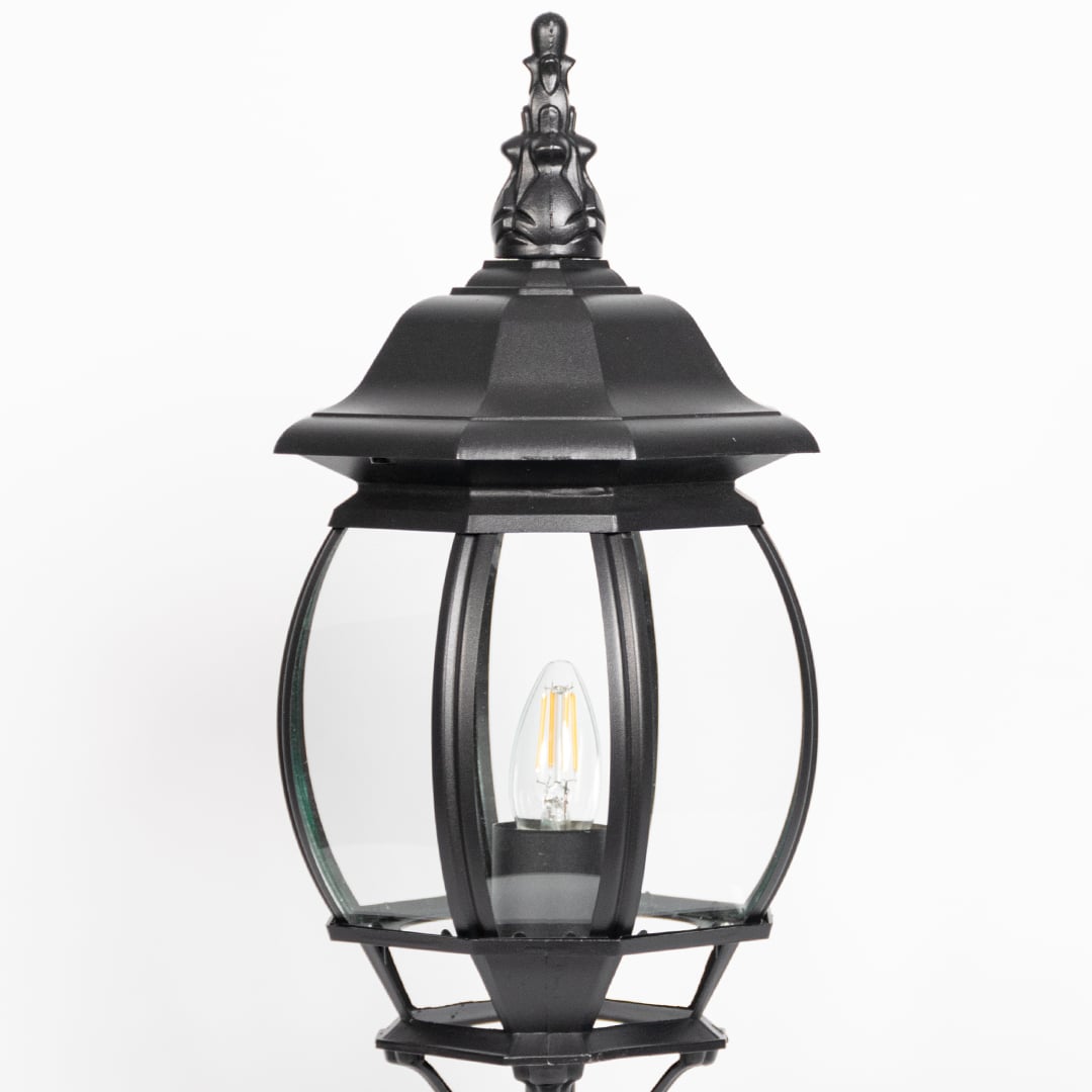 Closeup of decorative black pillar light with curved glass panels and LED bulb showcasing elegant outdoor lighting.