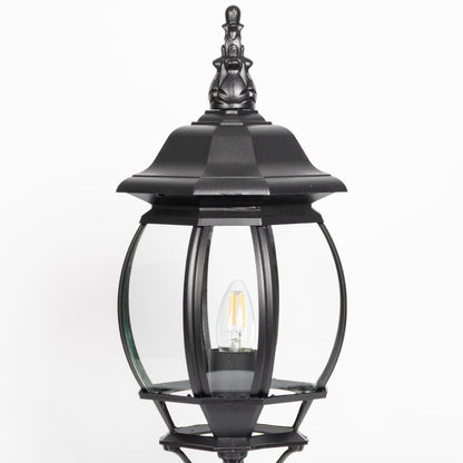 Closeup of decorative black pillar light with curved glass panels and LED bulb showcasing elegant outdoor lighting.