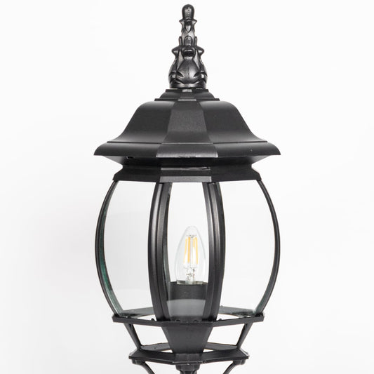 Closeup of decorative black pillar light with curved glass panels and LED bulb showcasing elegant outdoor lighting.