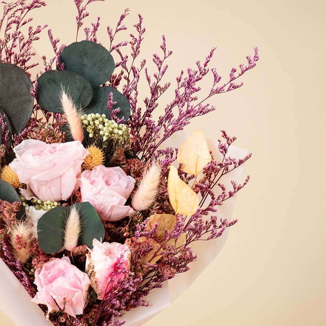 Closeup of elegant dried bouquet featuring light pink infinity rose bunny tail crystal grass rice flower and preserved leaves.