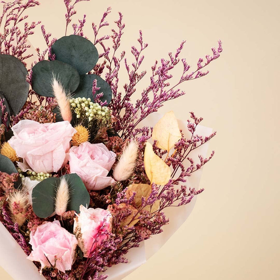 Closeup of elegant dried bouquet featuring light pink infinity rose bunny tail crystal grass rice flower and preserved leaves.