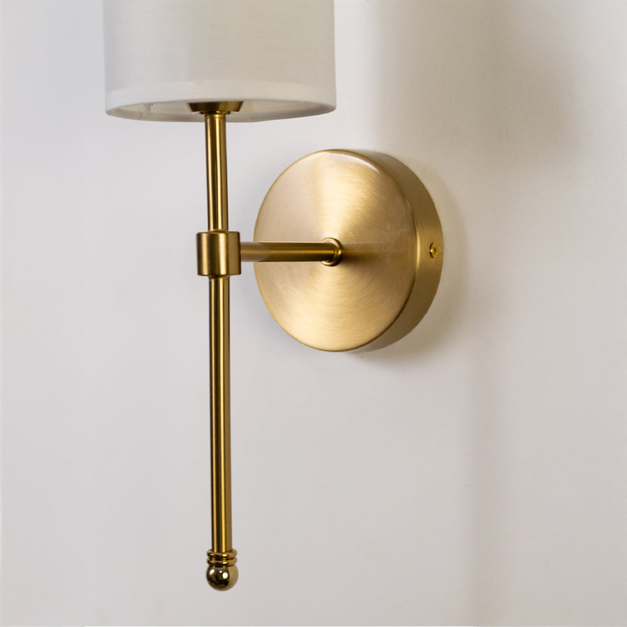 Modern wall light in gold metal finish with fabric shade for bedroom or living decor lighting placement white background.