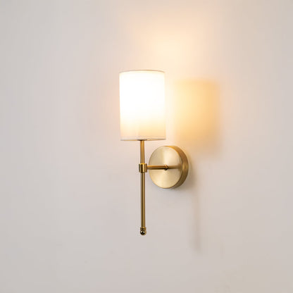Metal gold wall light with white fabric shade glowing softly on a clean white background ideal for bedroom or hallway wall lighting.