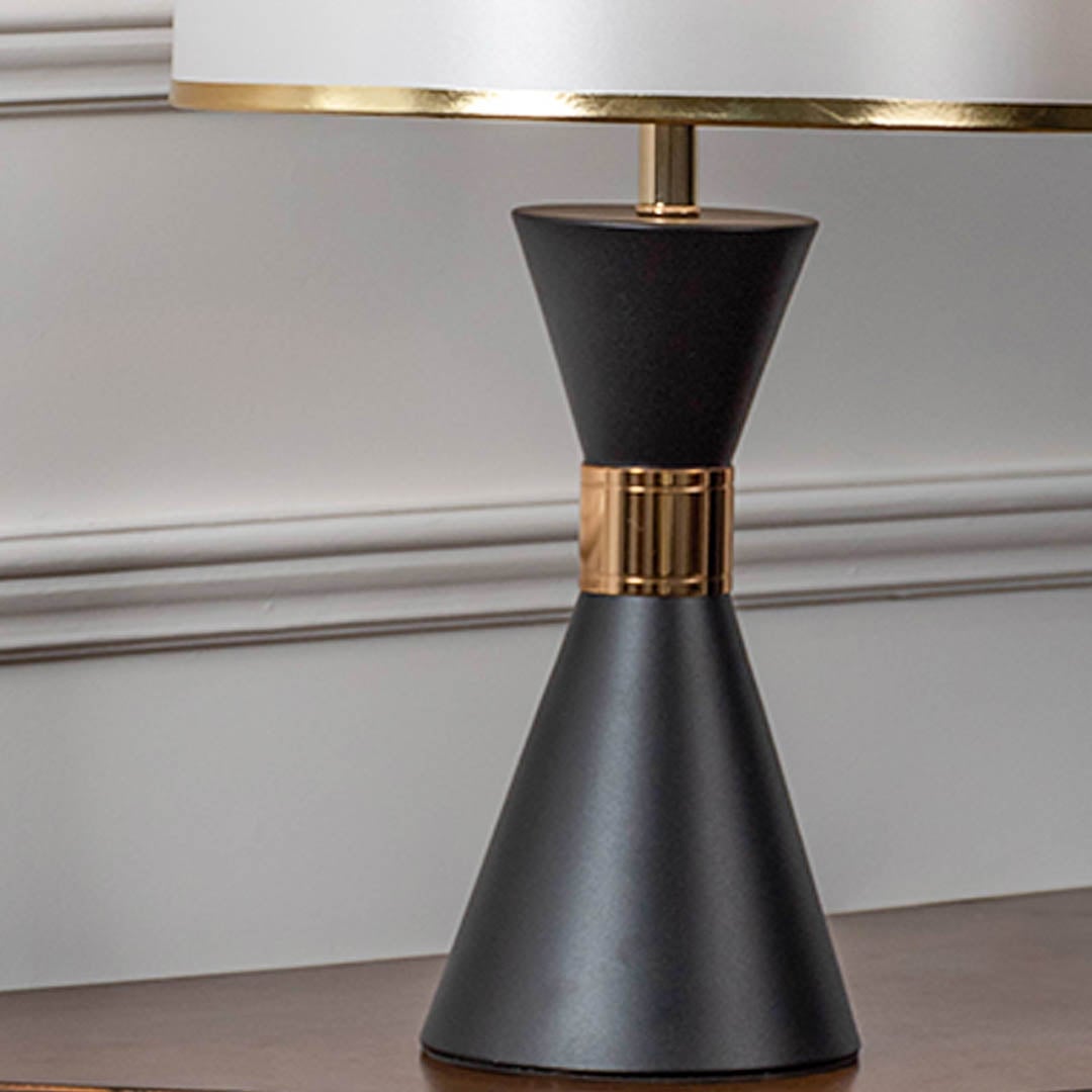 Closeup of black ceramic table lamp with golden detailing and drum style fabric shade showing modern decor design.