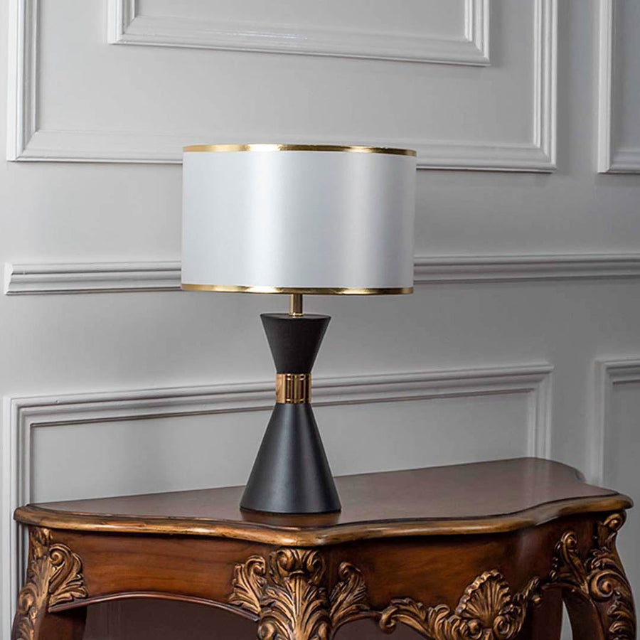 Black ceramic table lamp turned off with drum shade and golden accents displayed on plain white background.