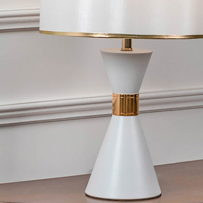 Closeup of white ceramic table lamp with glossy finish brass detailing and drum style lampshade for home decor.