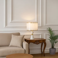 White ceramic table lamp with golden accents and fabric drum shade adding elegant lighting to modern living room.