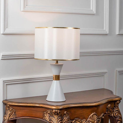 Table lamp with white ceramic base and wide fabric shade on wooden console table minimal classic lighting for home decor.