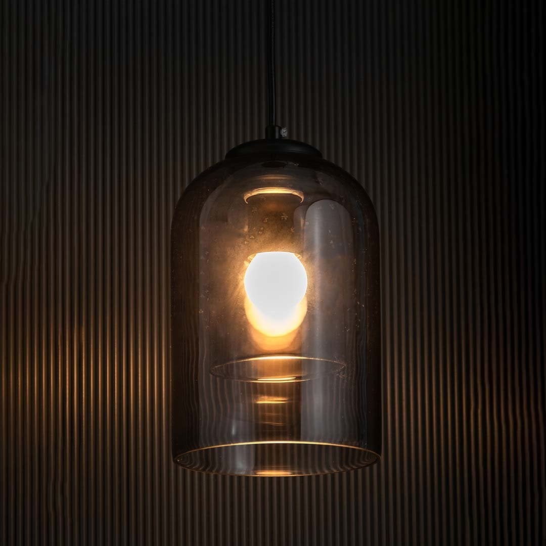 A smoked glass dome pendant light glowing warmly against a dark textured backdrop creating a rich ambient lighting effect for contemporary home styling.