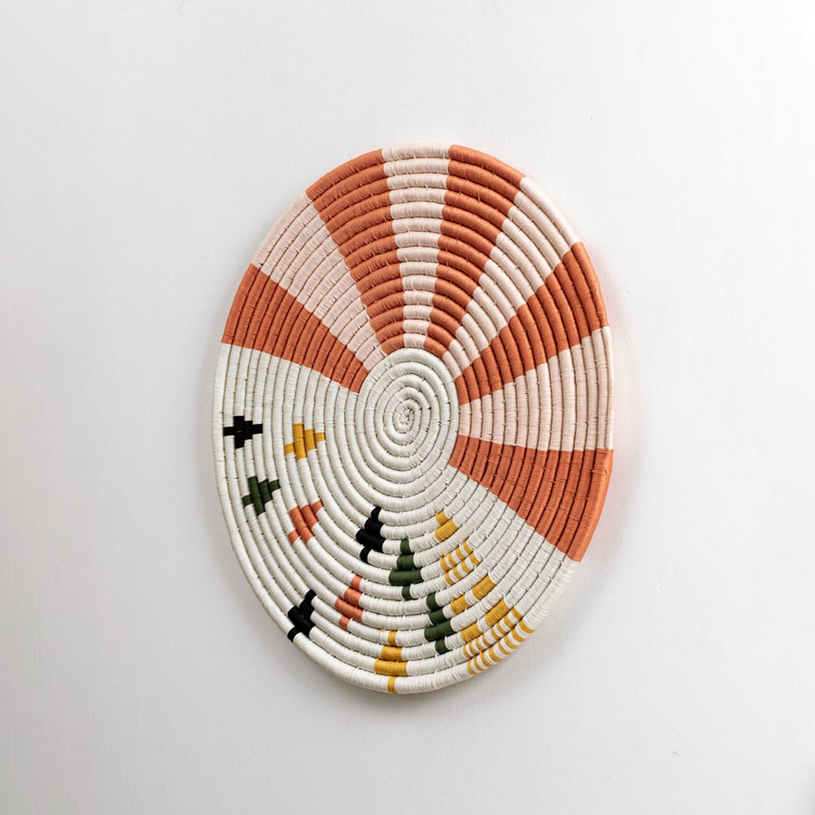 Round cotton woven wall plate with warm orange and cream detailing captured from a side angle on a dark background for stylish modern interior decor.