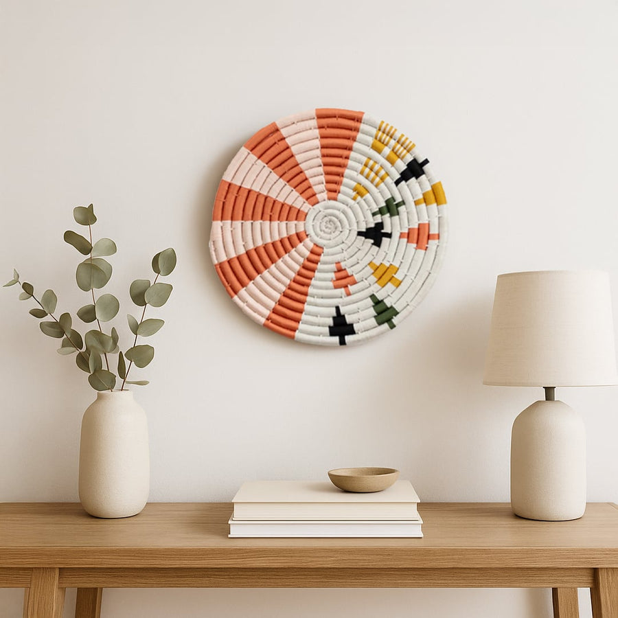 A multicolor woven wall plate styled above a wooden console with neutral decor accents creating a warm minimalist setting that highlights its textured handcrafted design.