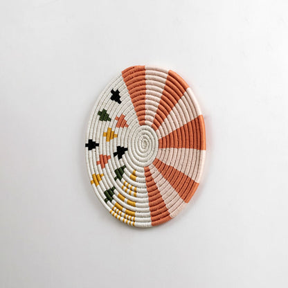 Round cotton woven wall decor in orange and cream tones captured from a side view on a dark background for modern artistic home styling.