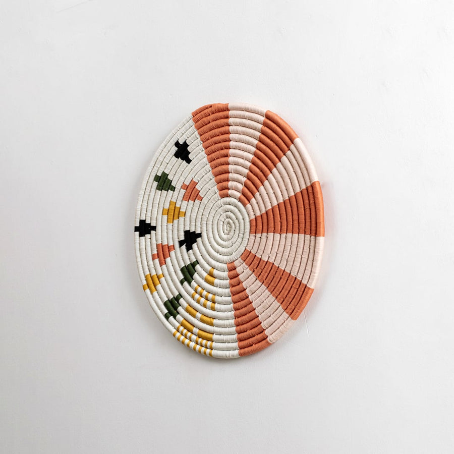 Round cotton woven wall decor in orange and cream tones captured from a side view on a dark background for modern artistic home styling.