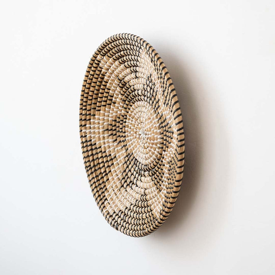 Side view of round woven wall basket highlighting layered thickness curved profile and handcrafted natural fiber detailing.