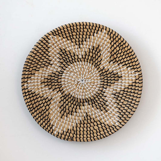 Handwoven wicker basket wall decor in beige with black and white starburst woven pattern design on clean white background.