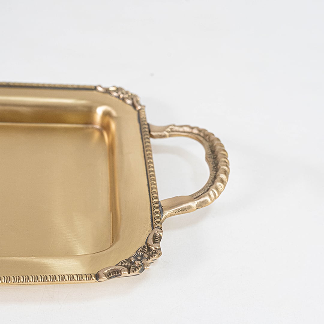 Gold rectangular metal tray with ornate handles displayed empty at an angle on a white background.