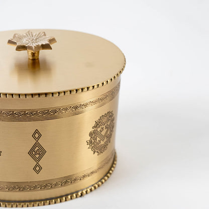 Open gold metal round storage jar with engraved details and lid placed beside it on plain white background.