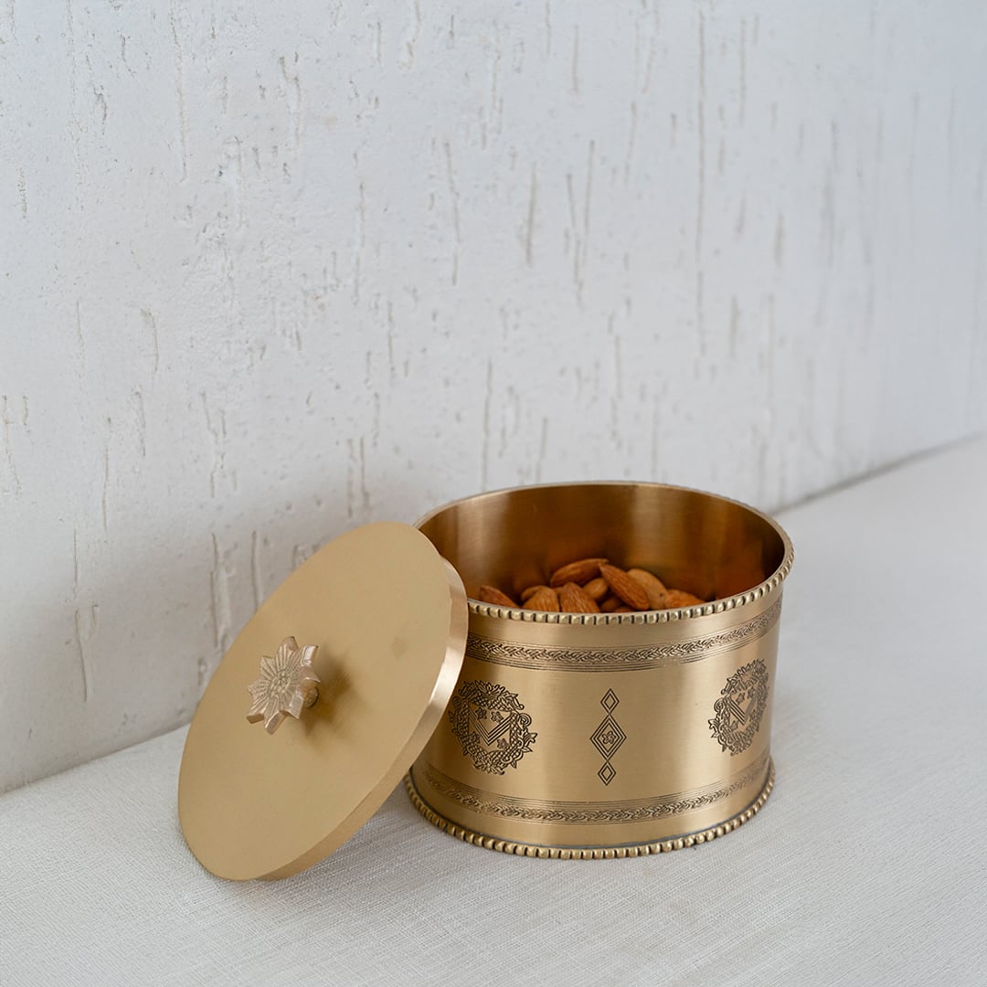 Gold metal storage jar with engraved design presented inside a black gift box with lid open for packaging display.