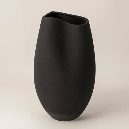 Handcrafted matte black ceramic vase with oval organic shape on white background highlighting elegant modern artistry.