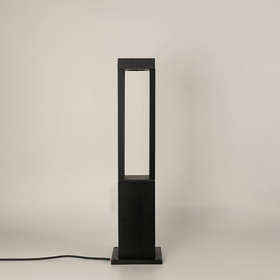 A modern black bollard light shown on a white background with the light off highlighting its open rectangular frame clean lines and sturdy base in a studio setting.