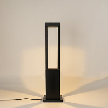 A contemporary black bollard light against a white background with the light on creating a warm focused glow that accentuates its minimal open frame structure.