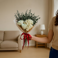 Elegant dried flower bouquet with white infinity rose hydrangea and eucalyptus wrapped with satin ribbon for home decor.