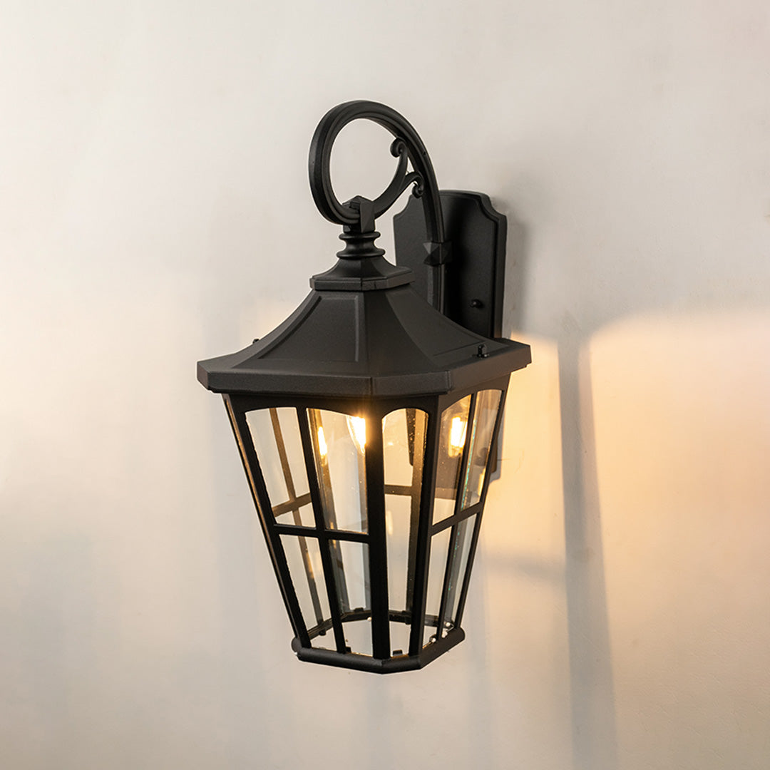 Black metal outdoor wall light on white background with tapered paneled clear glass shade for patio decor.