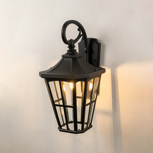 Black metal outdoor wall light on white background with tapered paneled clear glass shade for patio decor.