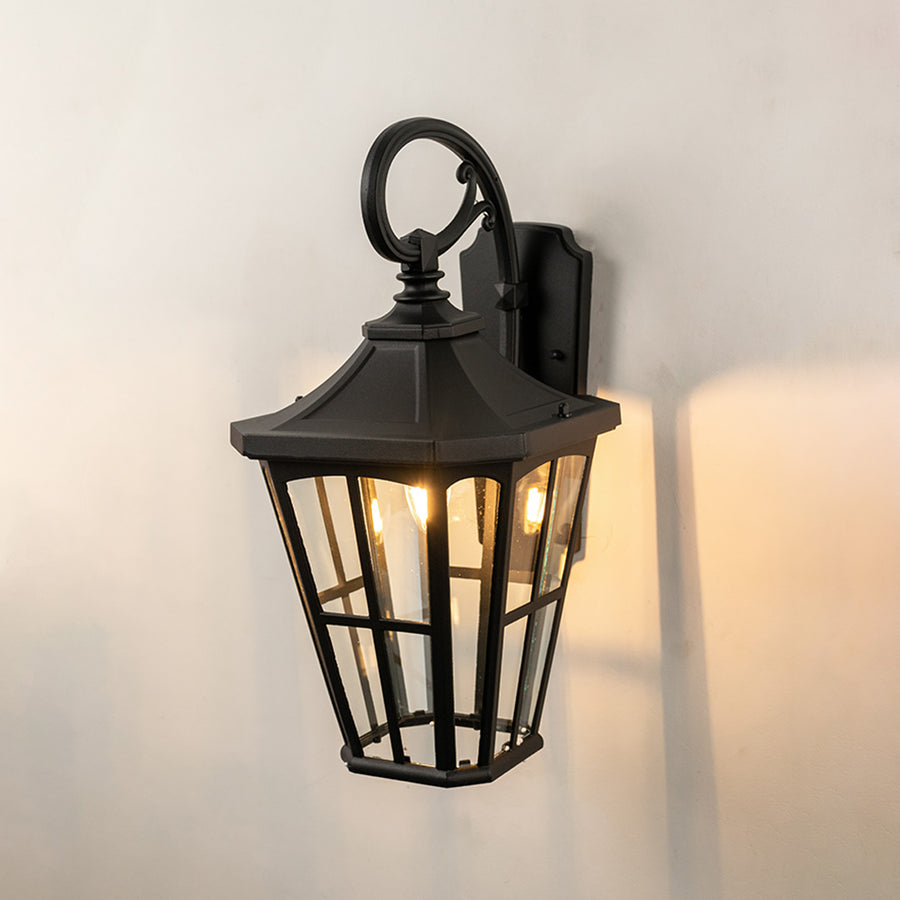 Black metal outdoor wall light on white background with tapered paneled clear glass shade for patio decor.